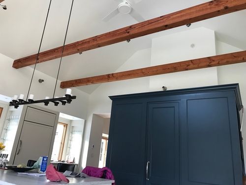 A kitchen with a chandelier hanging from the ceiling and wooden beams.