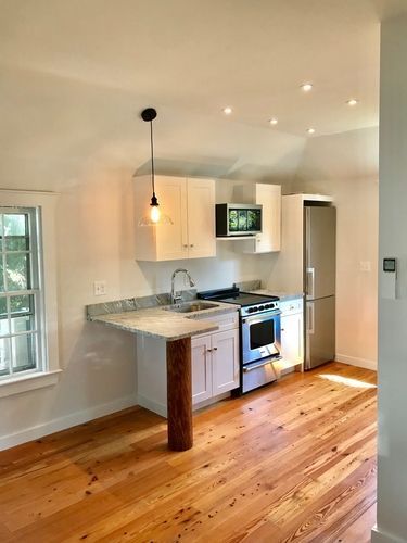An empty kitchen with wooden floors and white cabinets.
