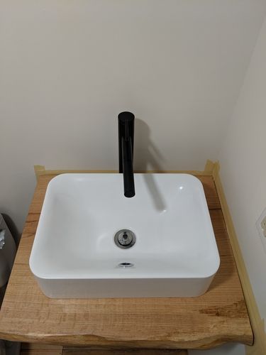 A white sink with a black faucet is sitting on top of a wooden counter.