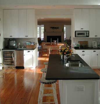 A kitchen with white cabinets , stools , a sink and a refrigerator.