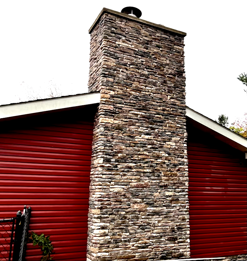 Stone chimney on a red-sided house with white roof trim