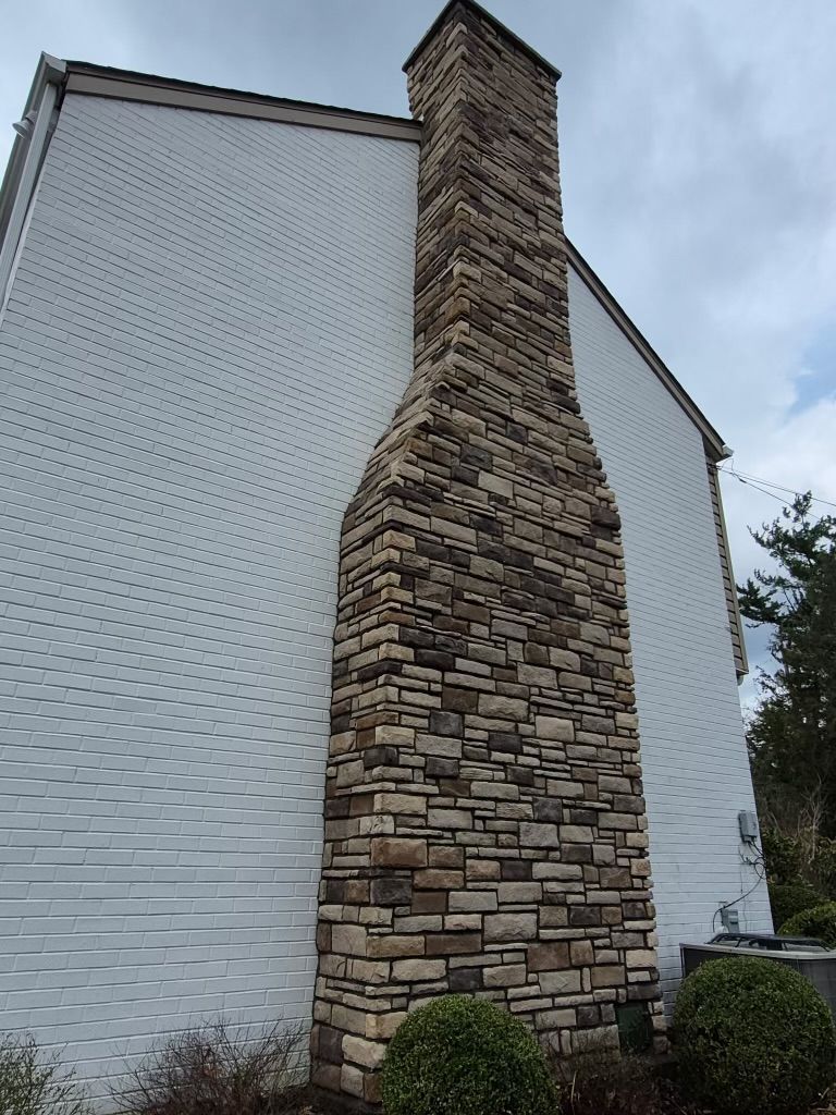 Stone chimney on the side of a white house under a cloudy sky.