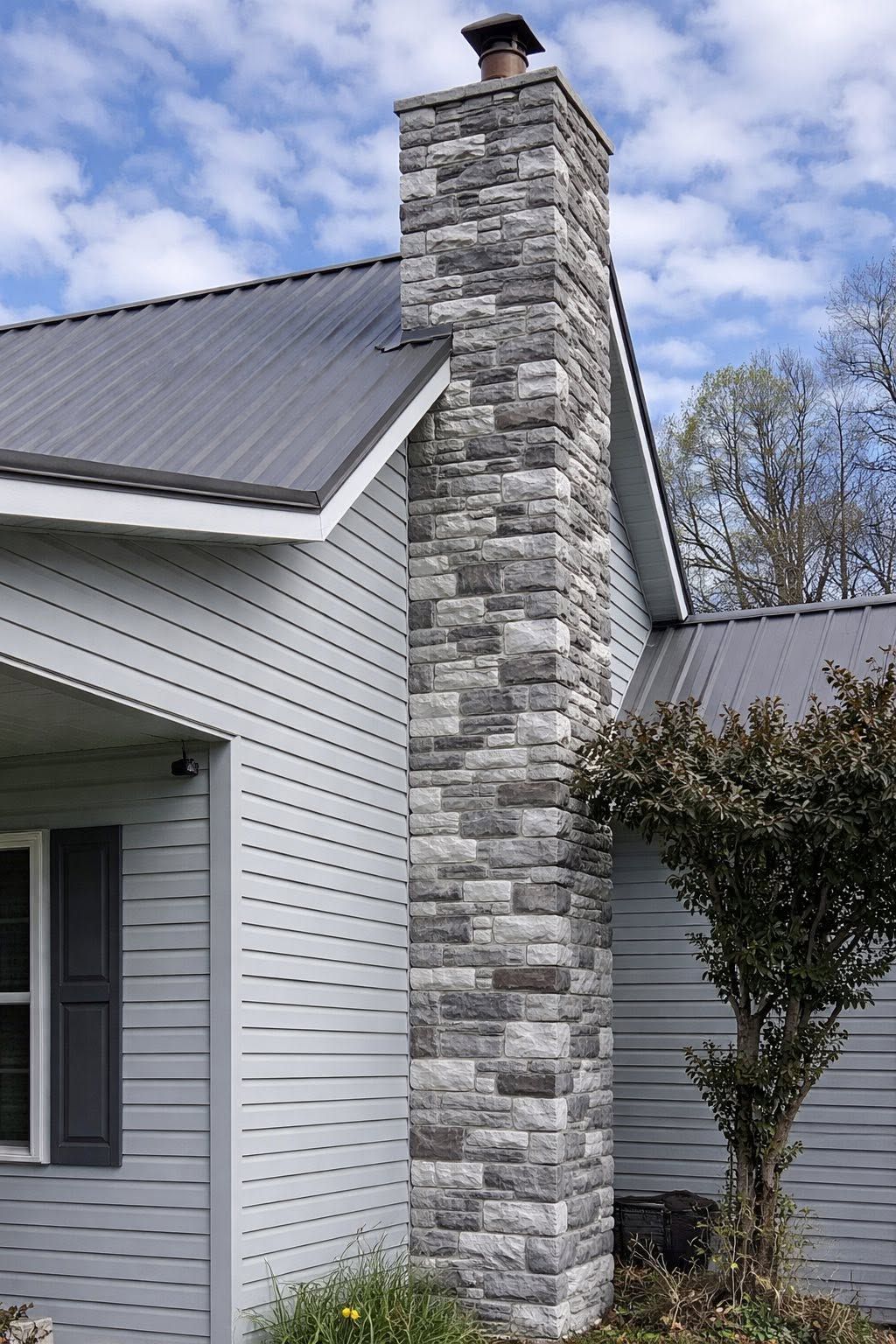 Stone chimney on a white house with a dark gray roof under a partly cloudy sky