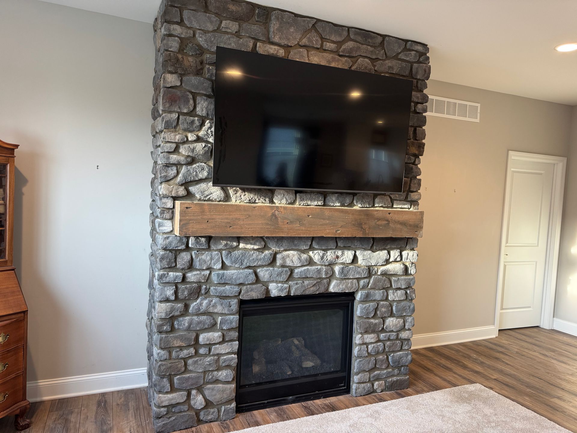 Living room with stone fireplace, mounted TV, and wood mantel on a light wall