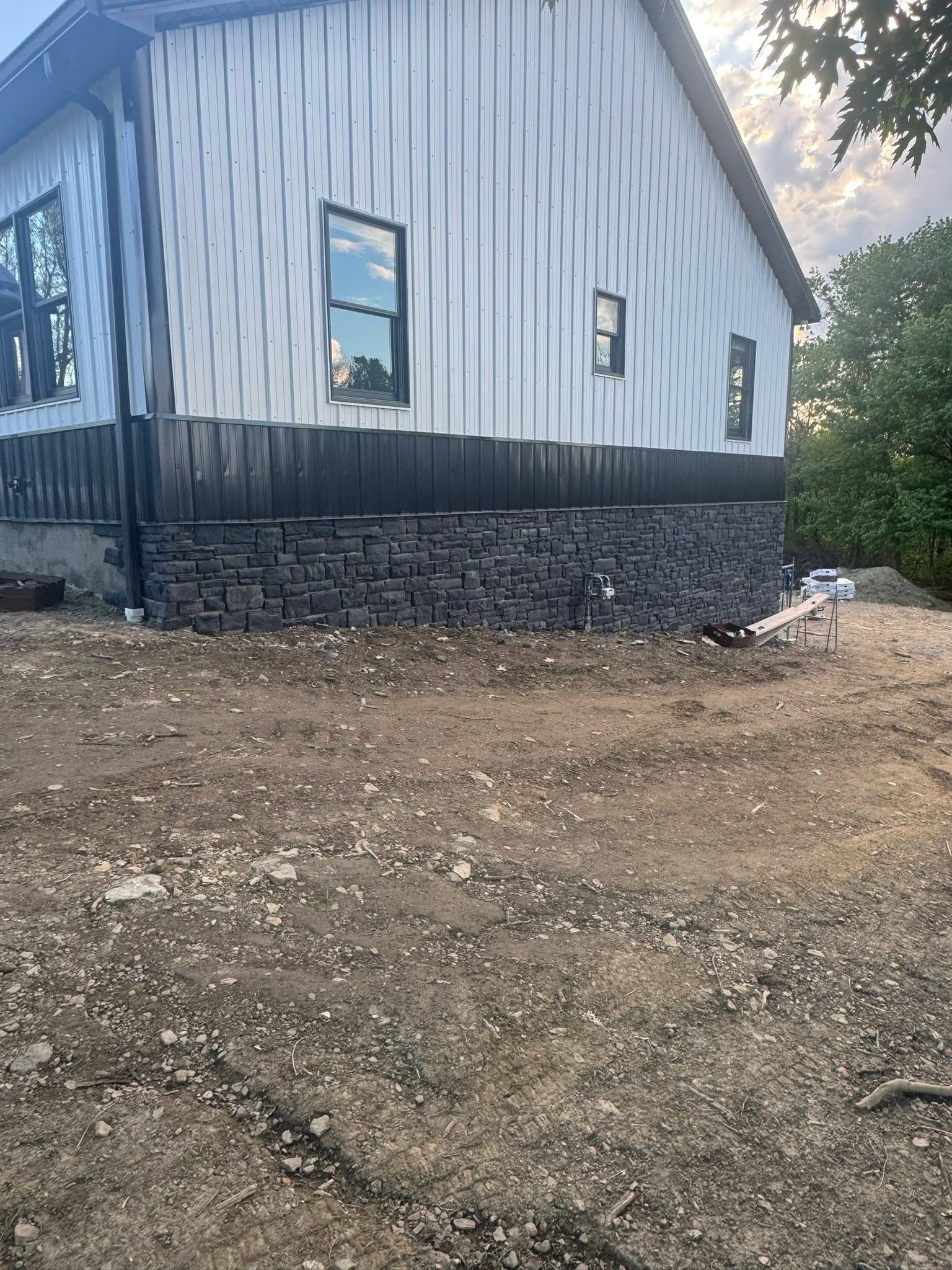 Metal-sided building with stone foundation on a gravel lot at dusk