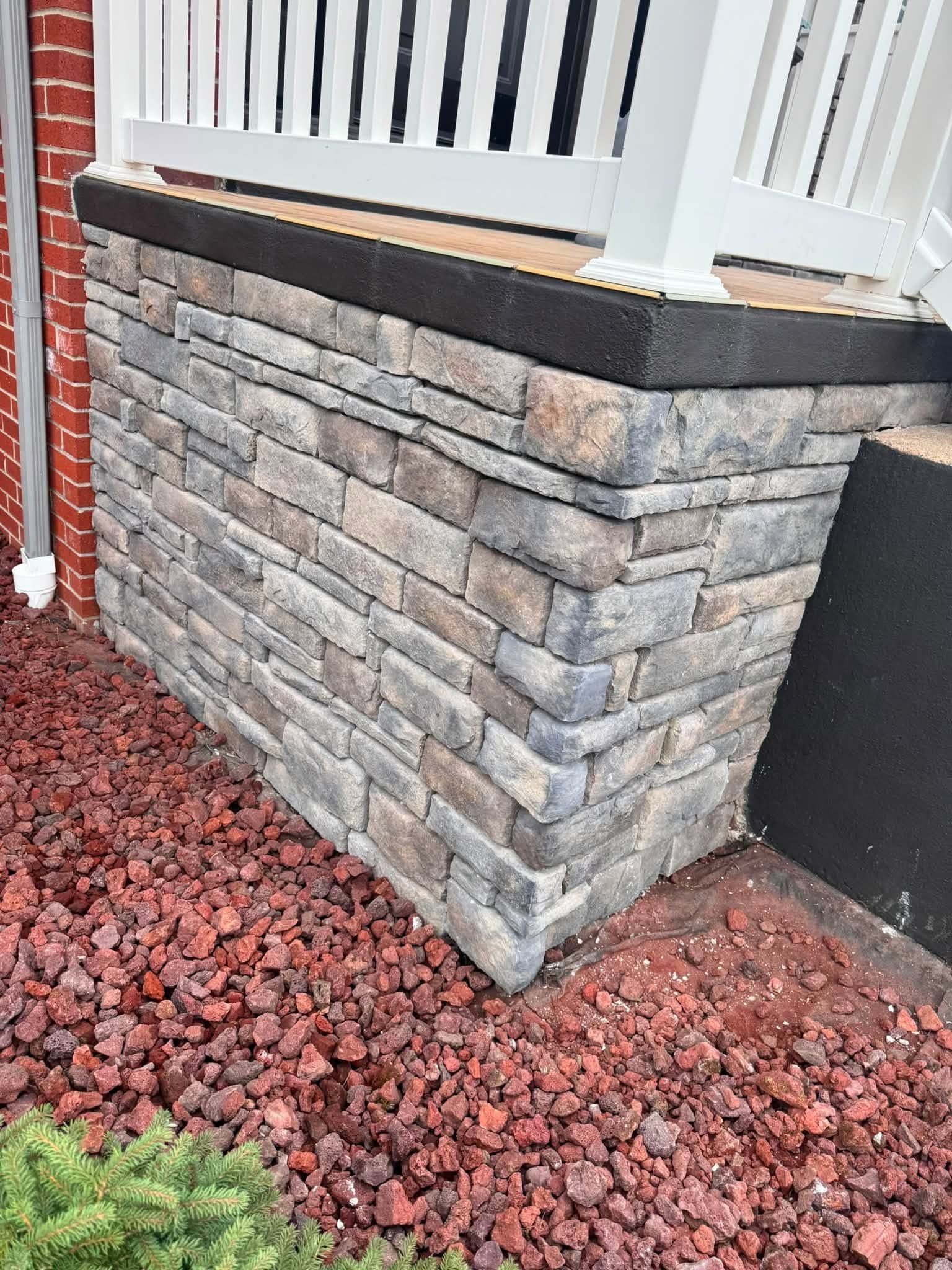 Stone-faced porch planter wall with black cap beside white railings and red gravel mulch