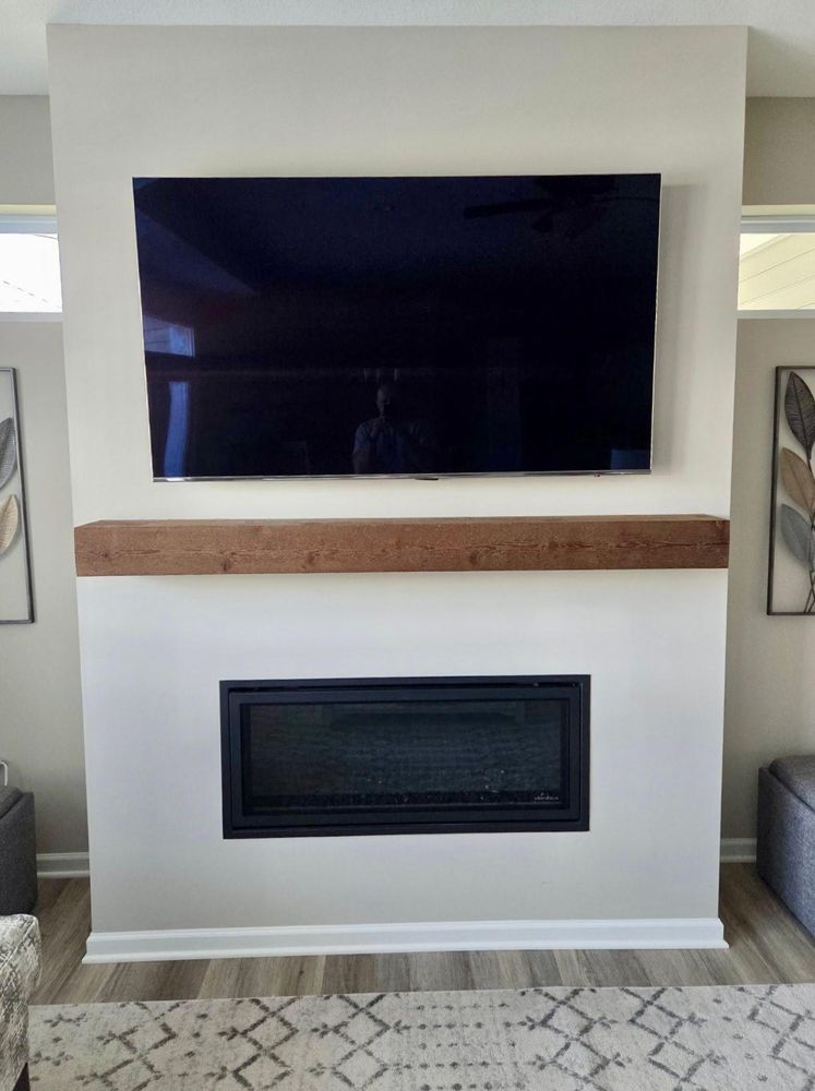 Living room wall with mounted TV above a fireplace and wooden mantel, flanked by framed art