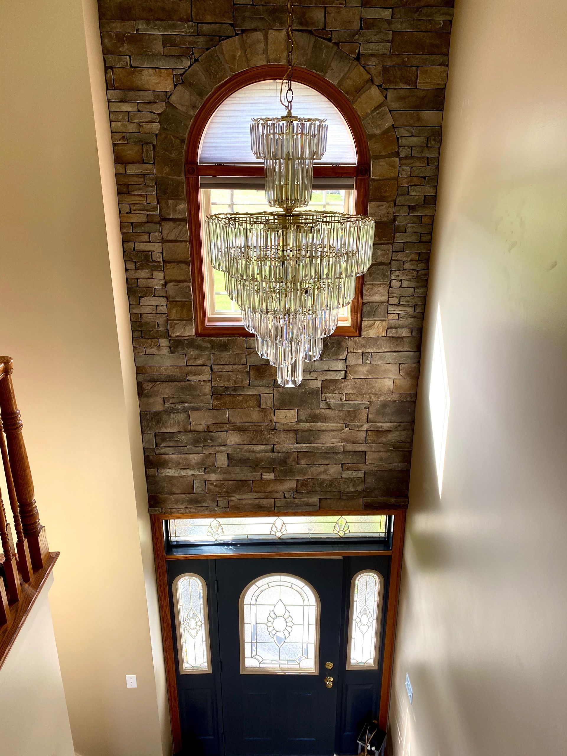 Grand foyer with crystal chandelier, brick accent wall, arched window, and dark front door.