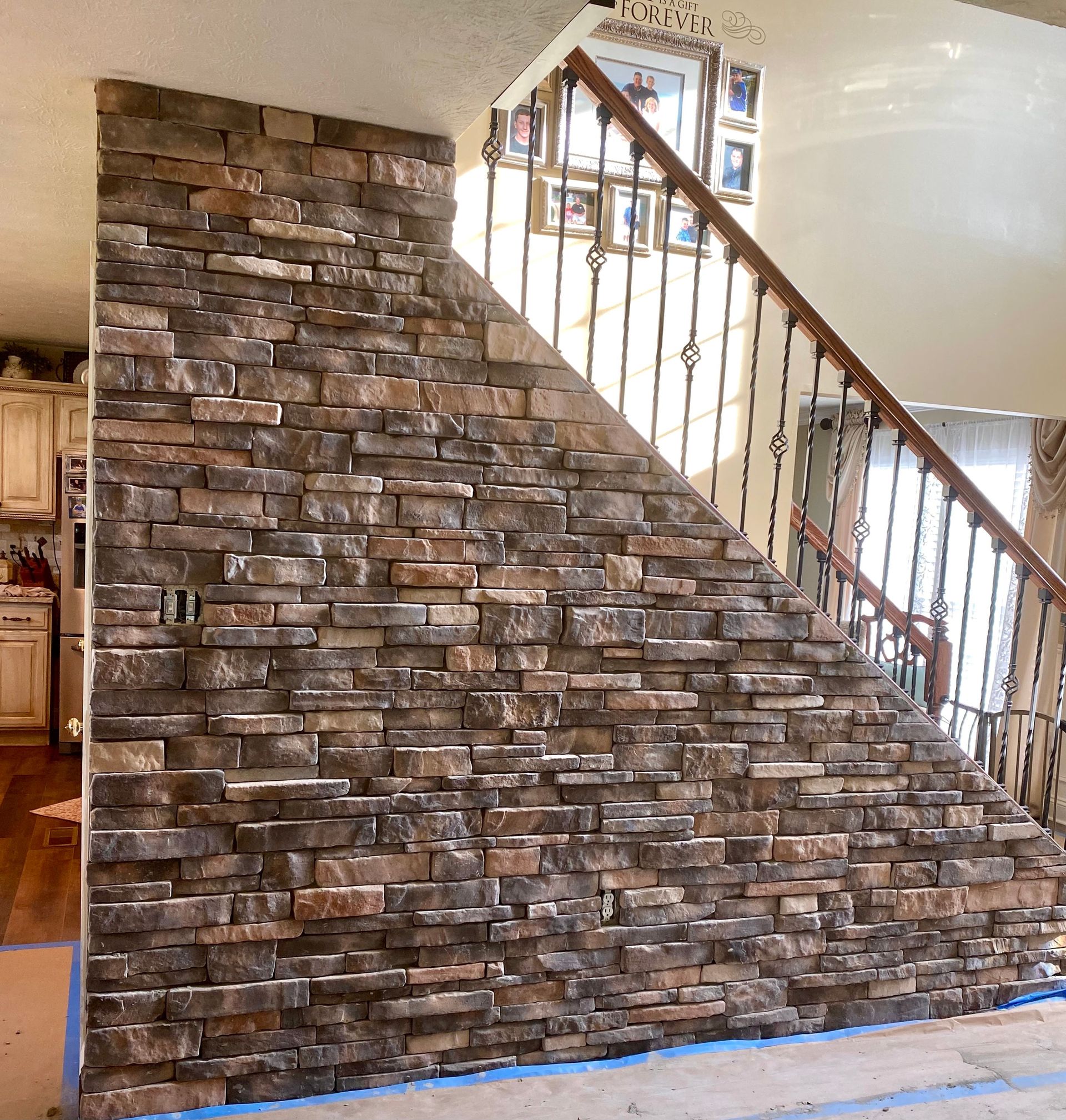 Stone-faced staircase wall inside a home, with wood railing and stairwell opening above.