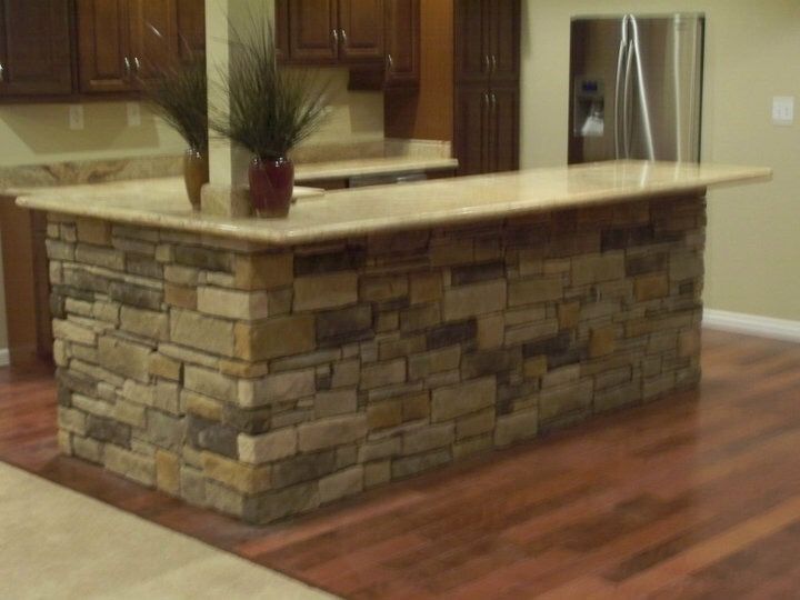 Kitchen island with stacked stone base, beige countertop, and hardwood floor in a modern kitchen