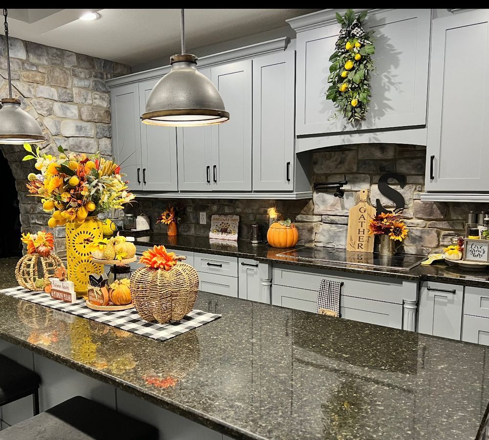 Decorated kitchen with autumn floral arrangements, pumpkins, and gray cabinets around a granite island