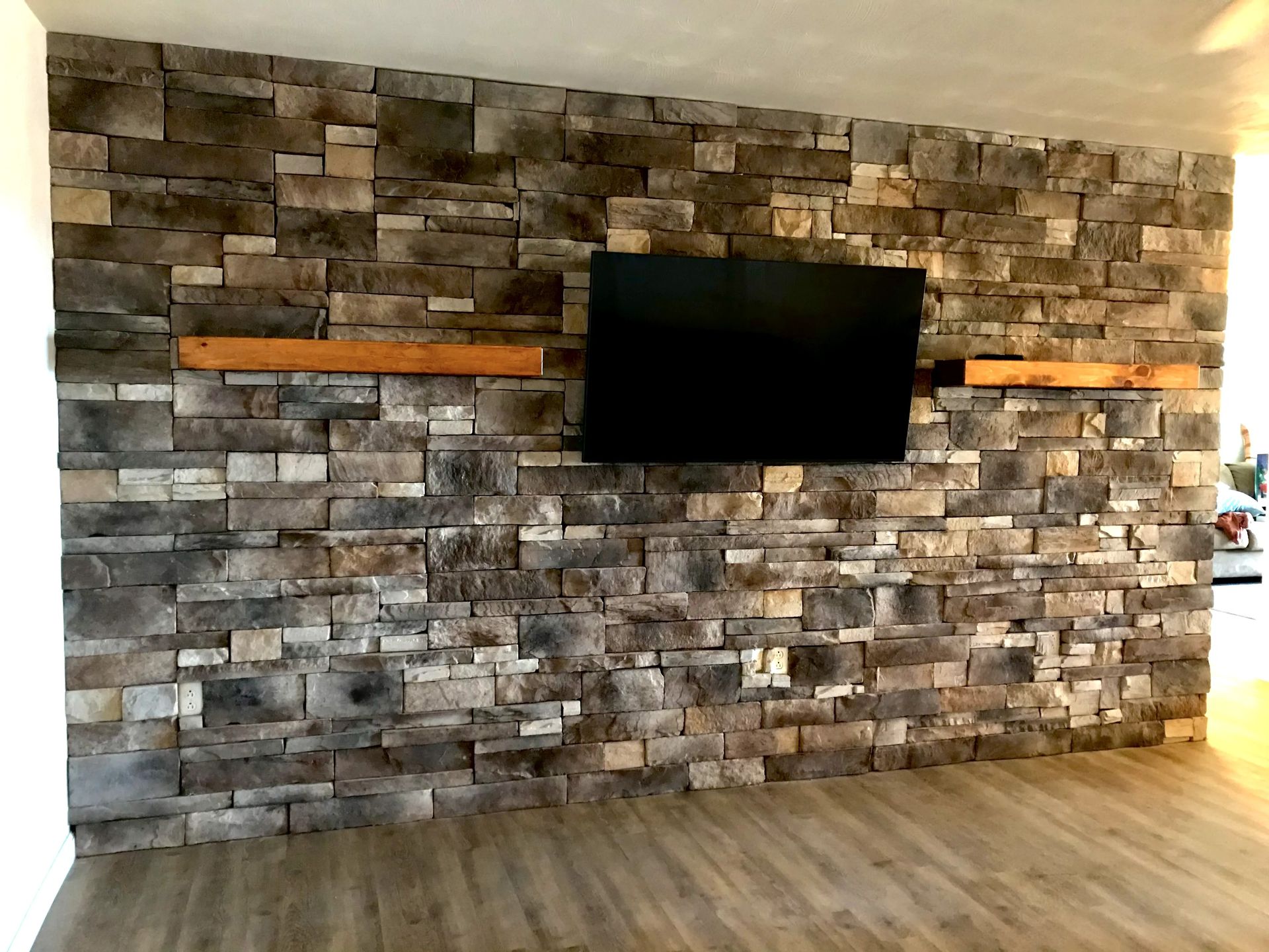 Stone accent wall with a wall-mounted TV and wood floor in a modern room