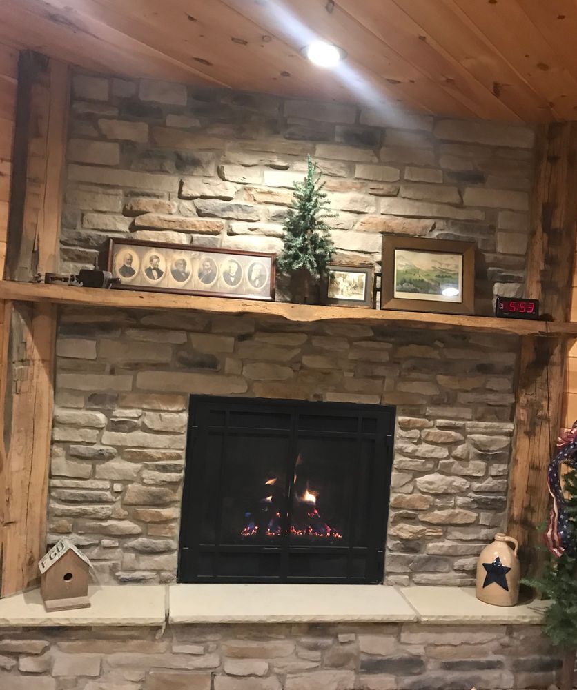 Cozy stone fireplace with a lit fire, wood mantel, framed decor, and a small Christmas tree above it.