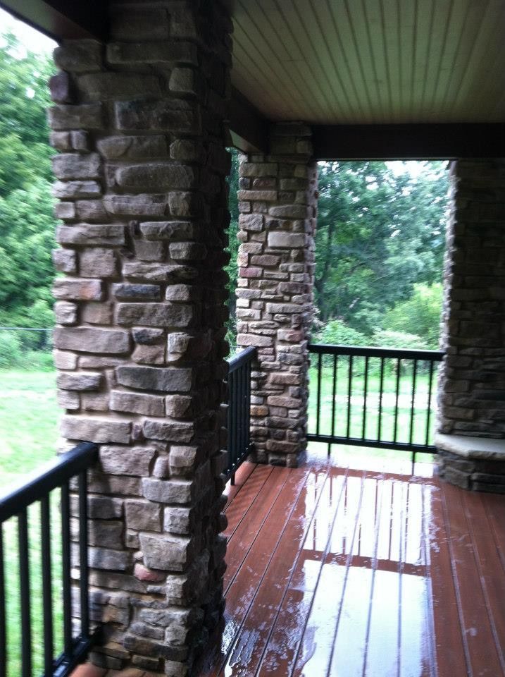 Covered stone porch with wooden floor and railing overlooking green trees