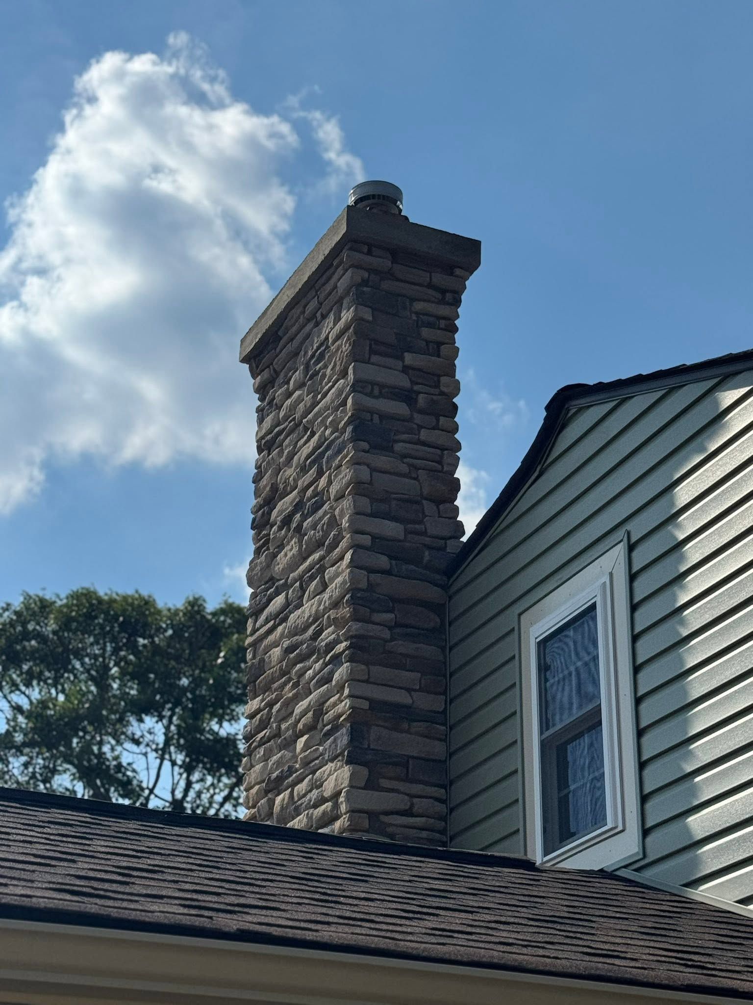 Stone chimney on a shingled house against a blue sky with clouds