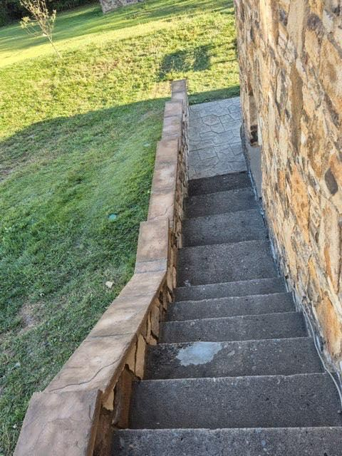 Stone outdoor staircase beside a grassy slope and stone wall, descending downhill.