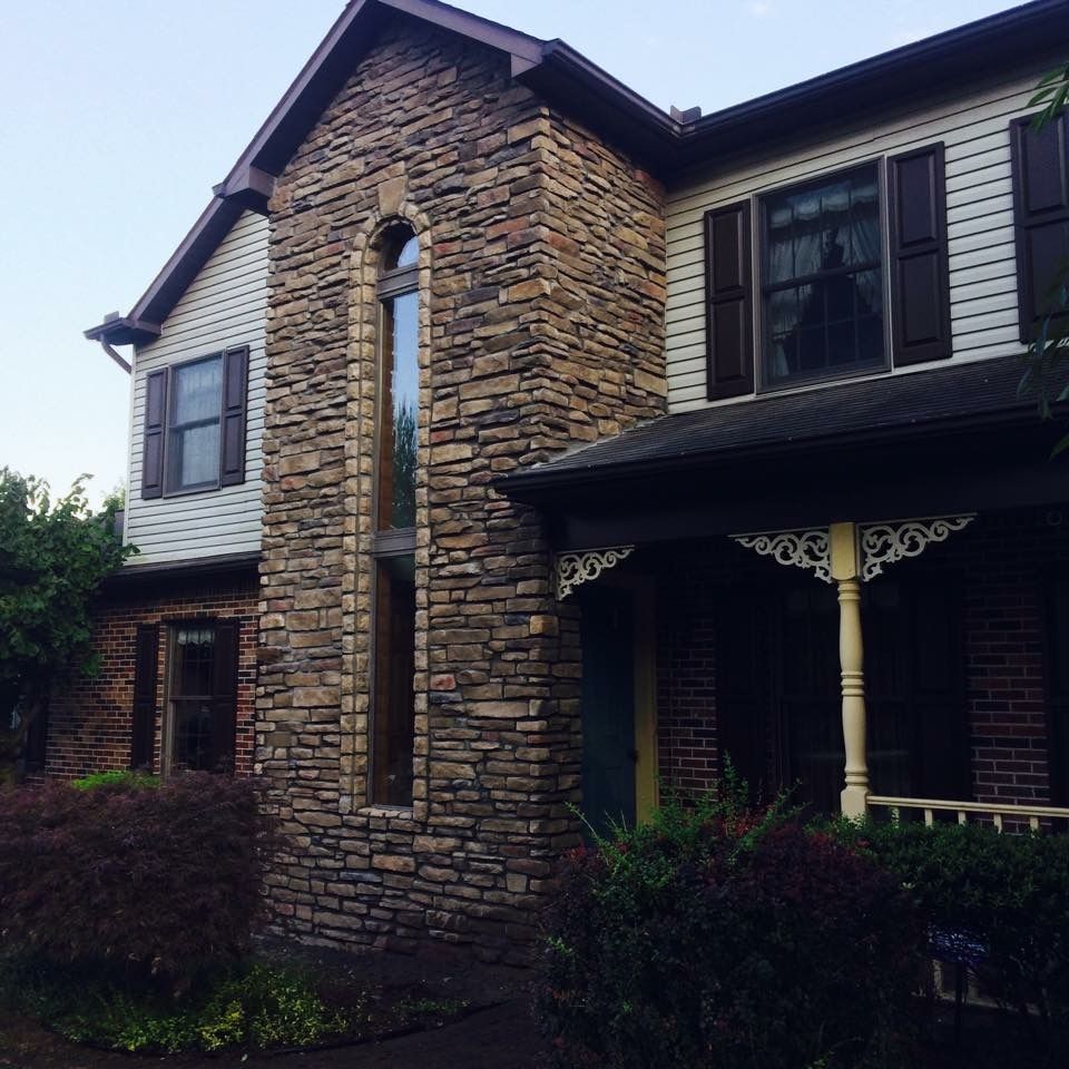 Stone-front suburban house with dark shutters, porch, and brick sides