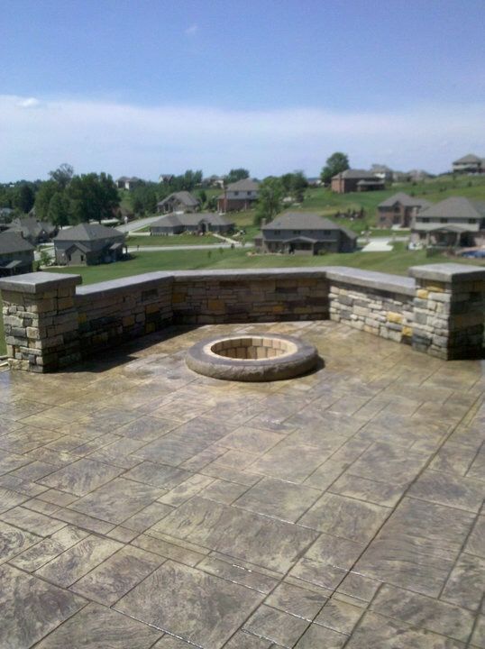 Stone patio with a circular fire pit overlooking suburban houses under a blue sky