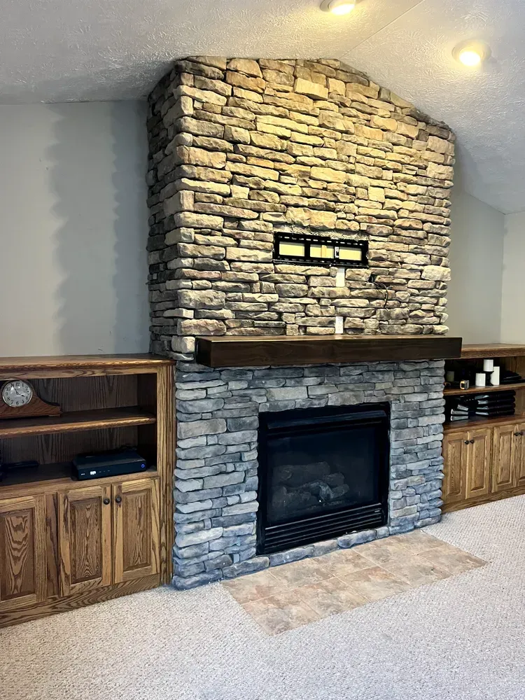 Stone fireplace with black insert, built-in wooden cabinets, and a beige carpeted living room wall
