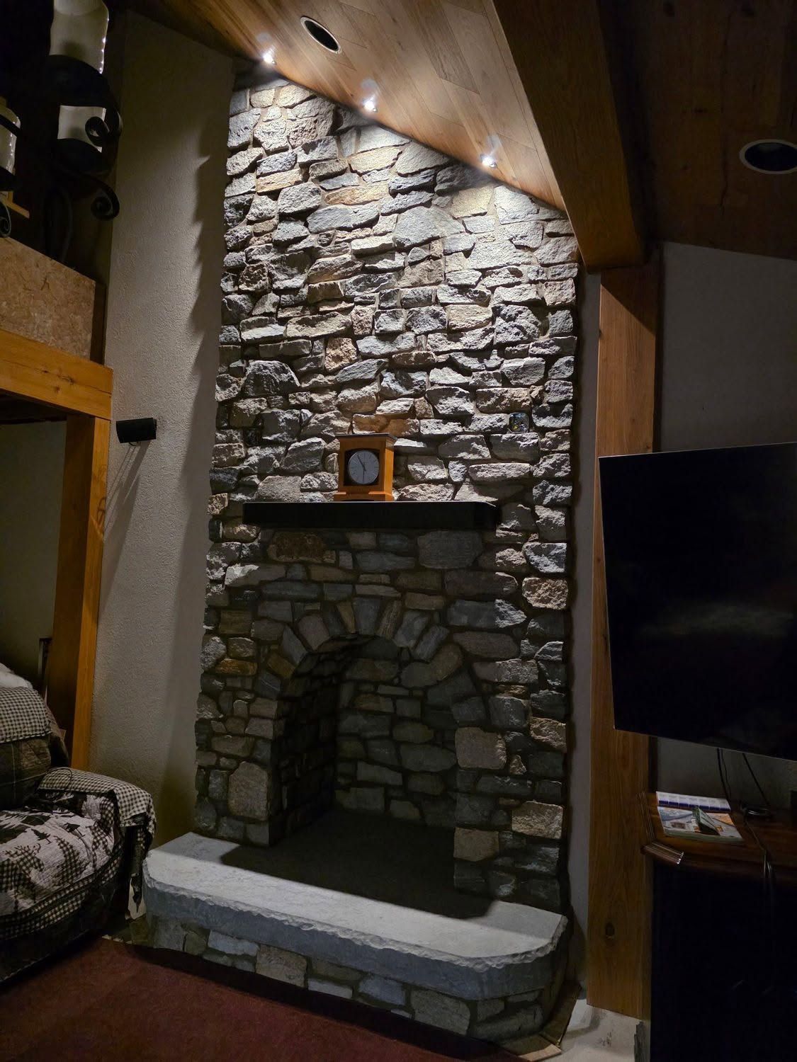 Stone fireplace in a rustic living room with a wood mantel and TV beside it