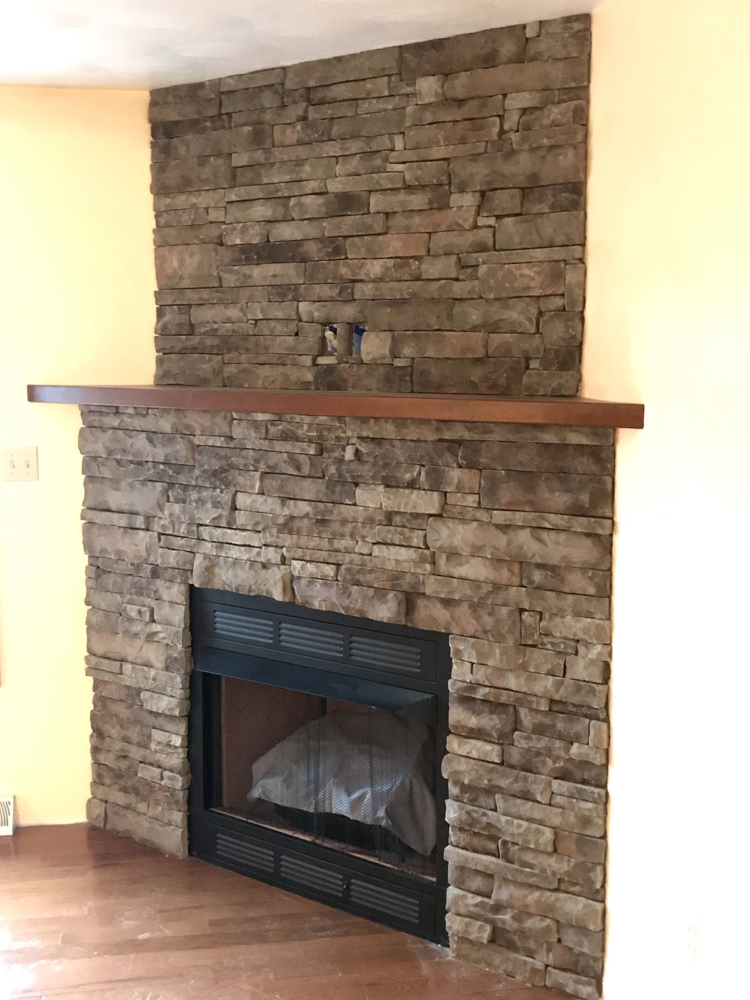 Stone fireplace with wooden mantel and black insert in a cream-walled room