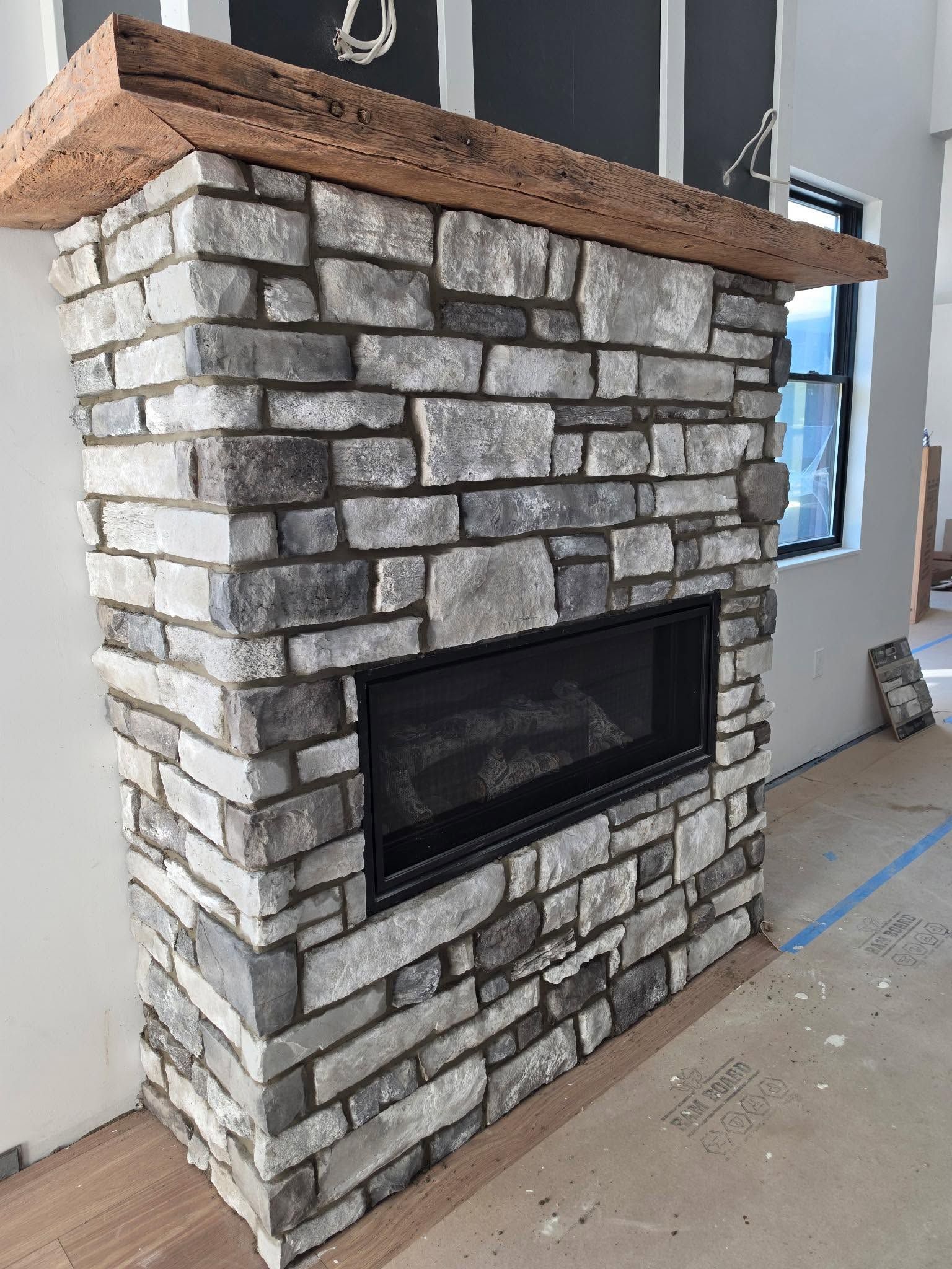 Stone fireplace with black insert and wood mantel in an unfinished room