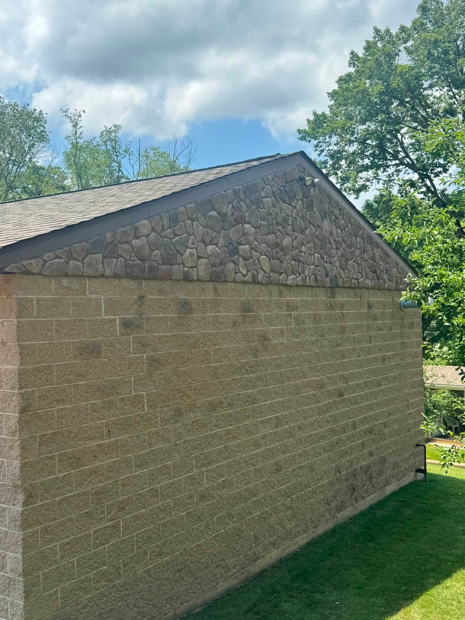 Side of a tan brick building with a stone gable roof under a blue, cloudy sky.