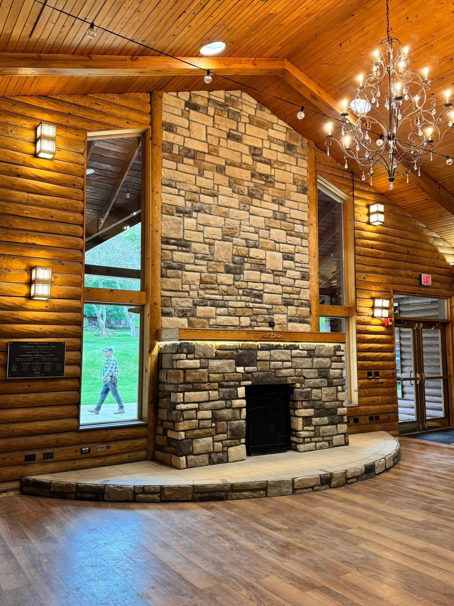 Rustic lodge lobby with stone fireplace, wood-paneled ceiling, chandelier, and polished floor