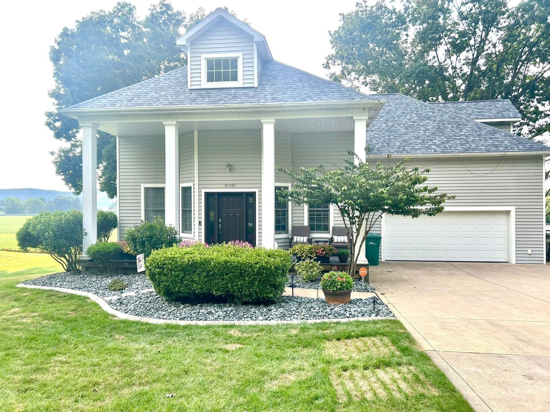 Small white house with front porch, black door, attached garage, and a manicured lawn