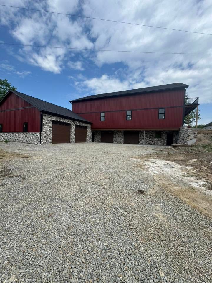 Red barn and garage on a gravel lot under a cloudy sky