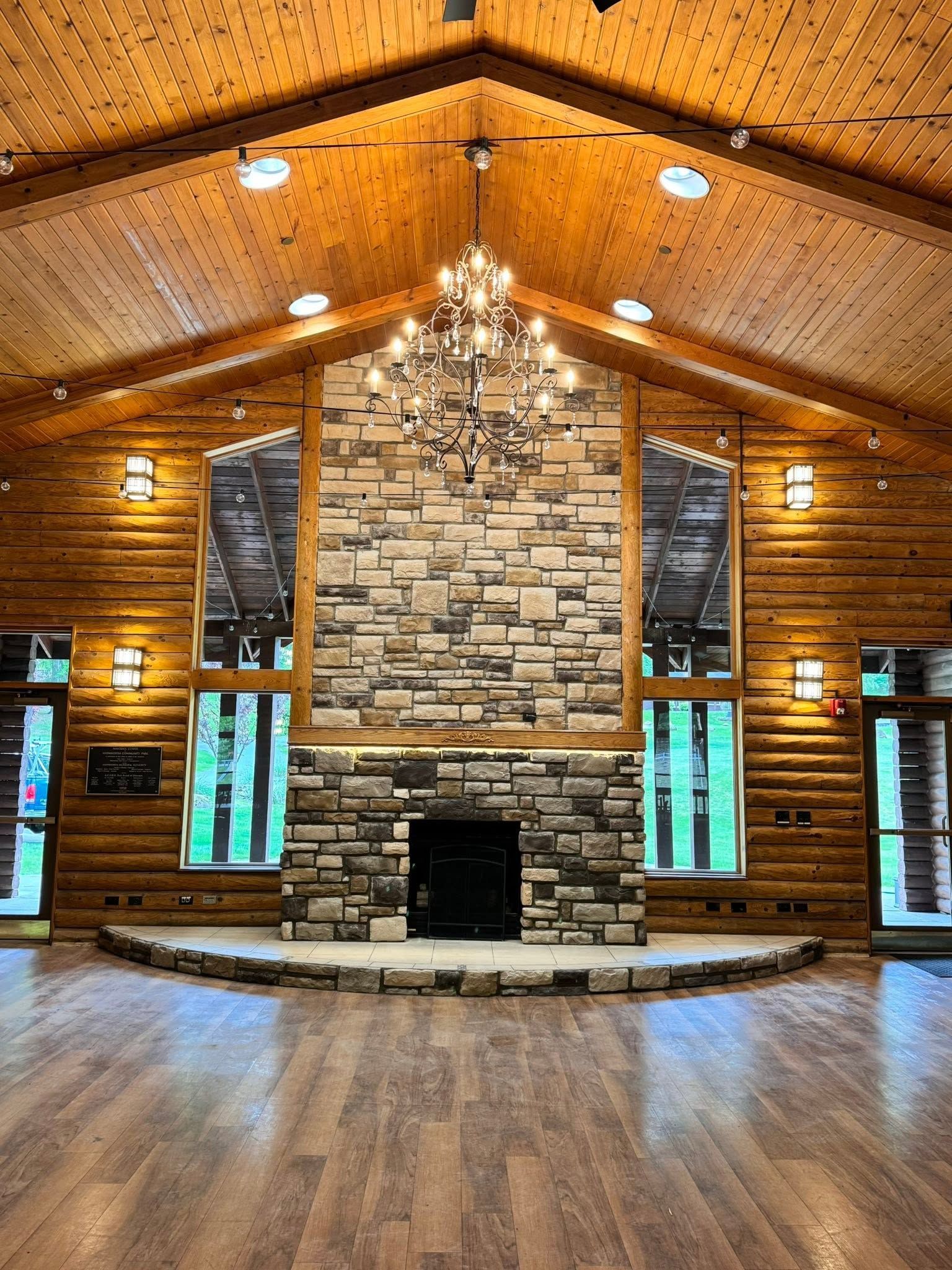 Wood-paneled lodge interior with stone fireplace, chandelier, and vaulted ceiling