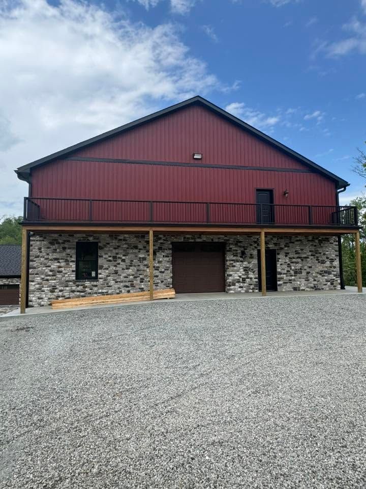 Red barn-style building with stone lower walls and a gravel forecourt under a cloudy sky