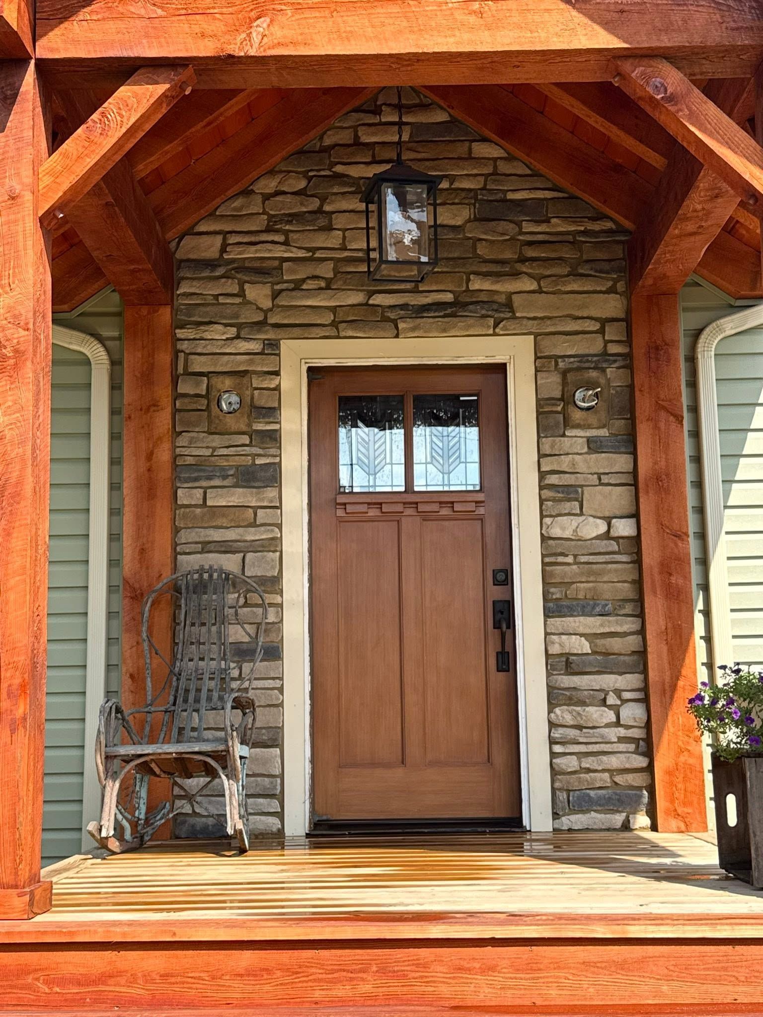 Rustic stone entryway with a wooden front door under a timber porch