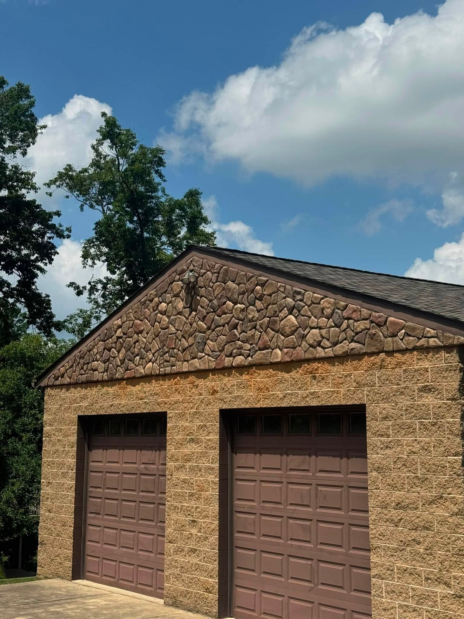 Stone garage with two brown doors and a tiled roof under a blue sky with clouds