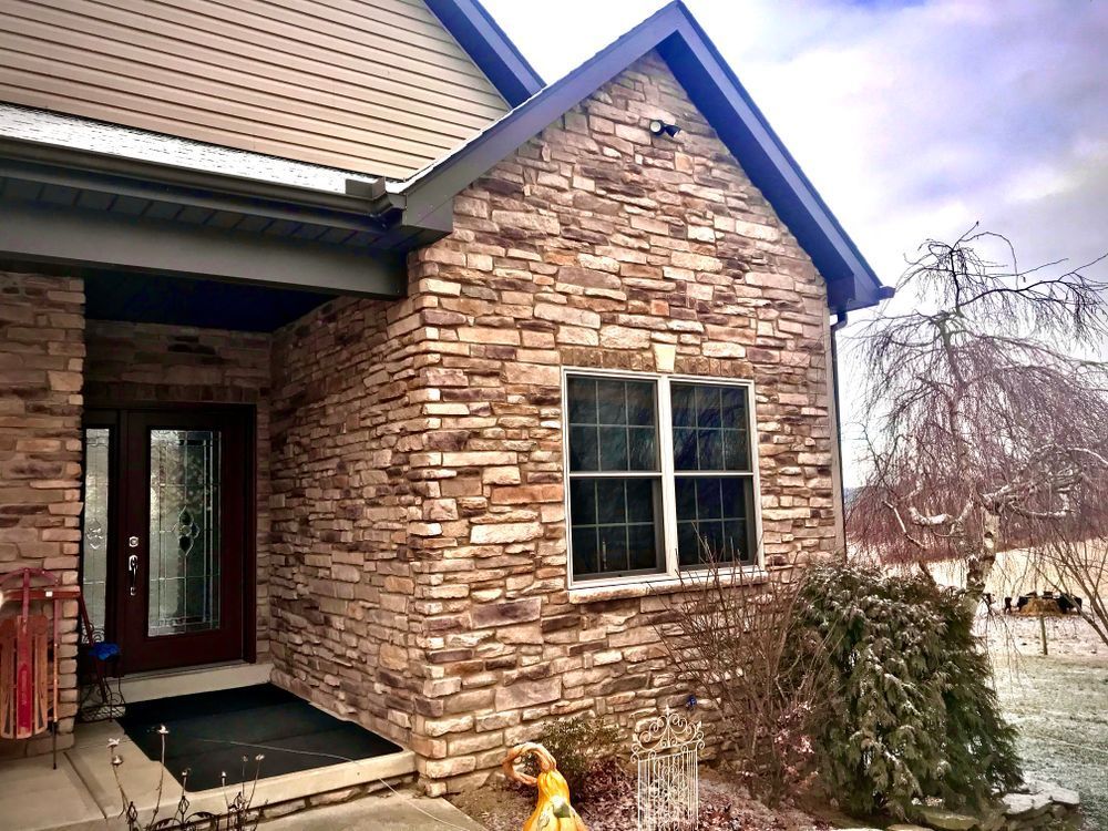 Stone-front house entry with a window, porch, and snowy yard.