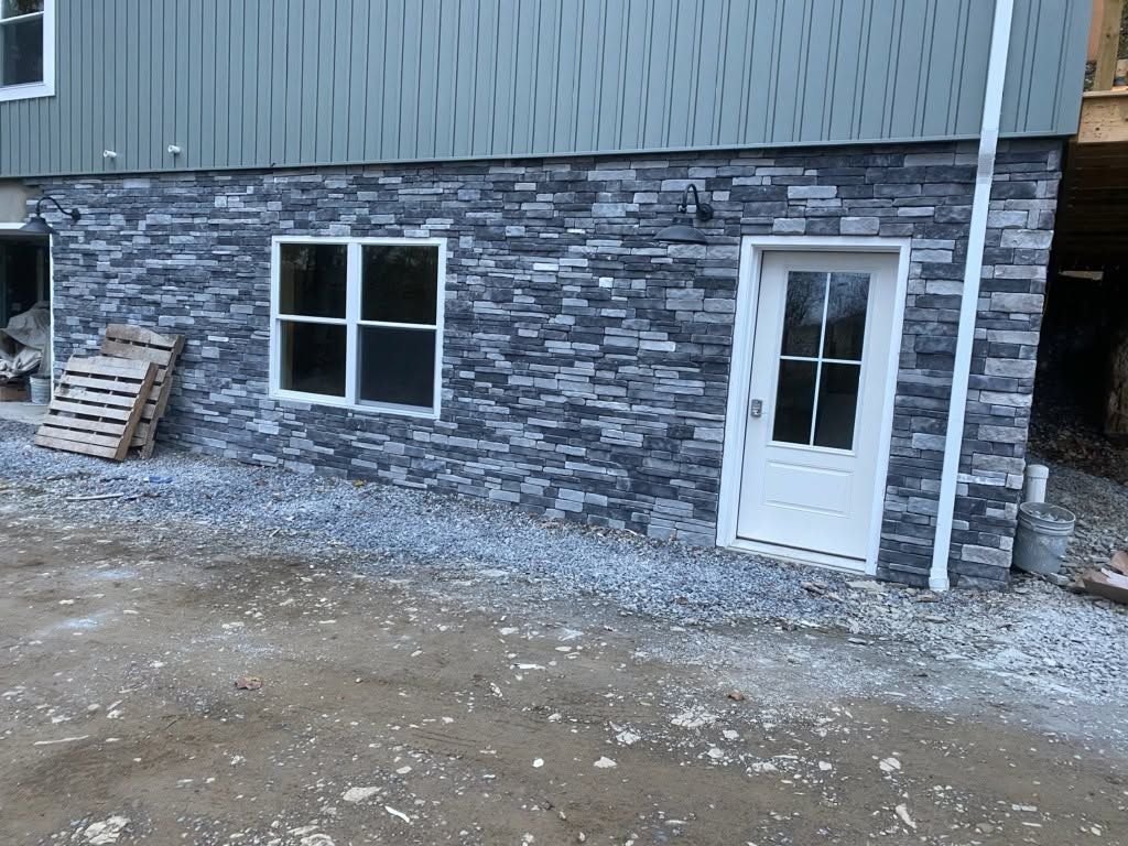 Stone-sided building exterior with a white door and window beside a gravel ground area