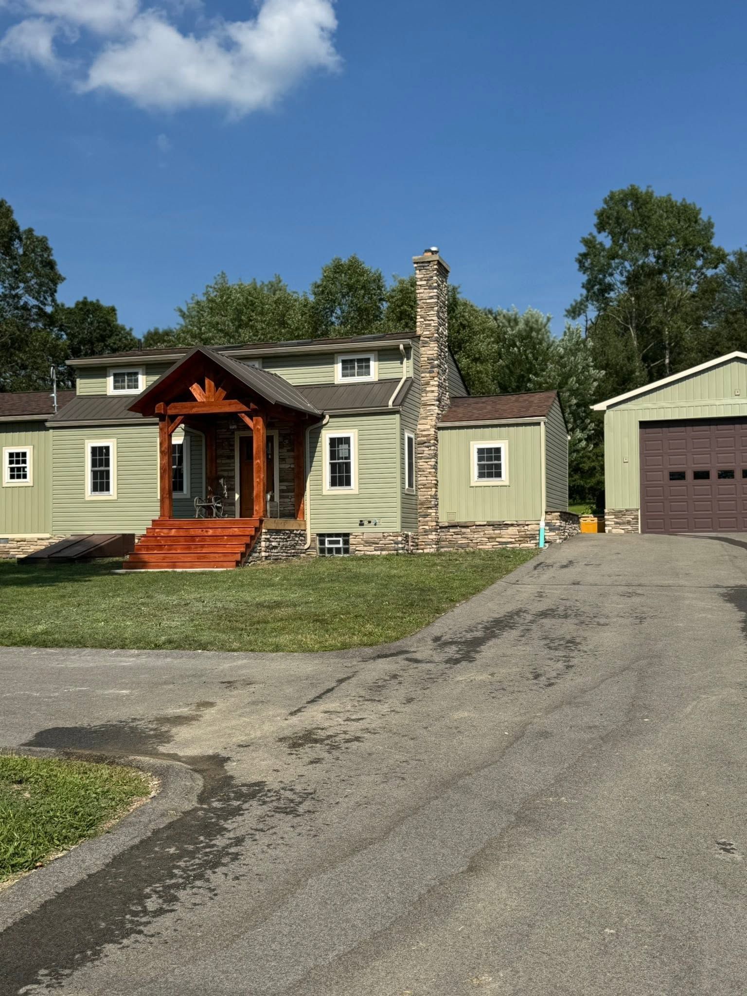 Single-story beige house with orange front porch, stone chimney, and attached garage under a clear blue sky