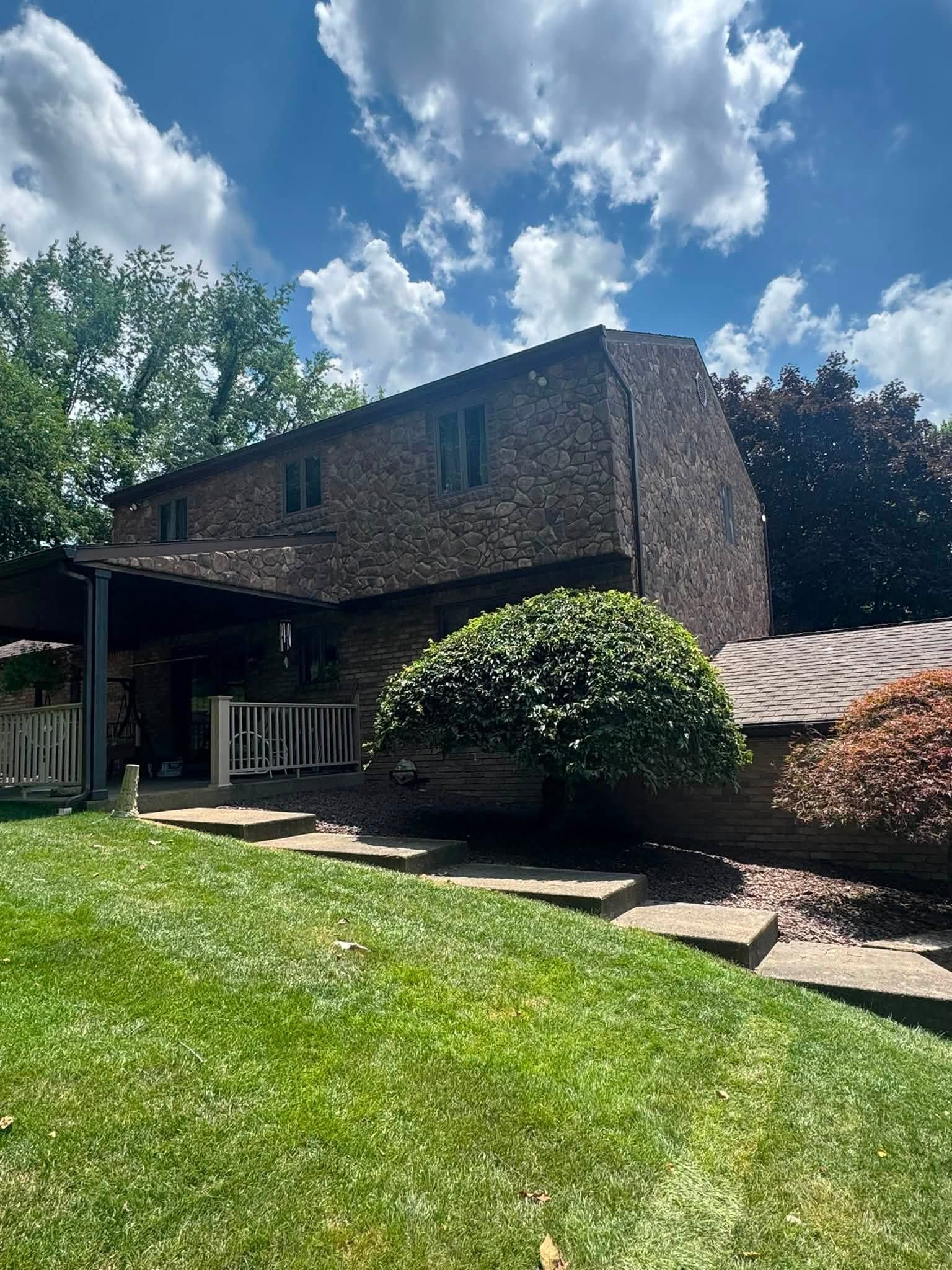 Two-story brick house with a green lawn, trees, and a partly cloudy blue sky