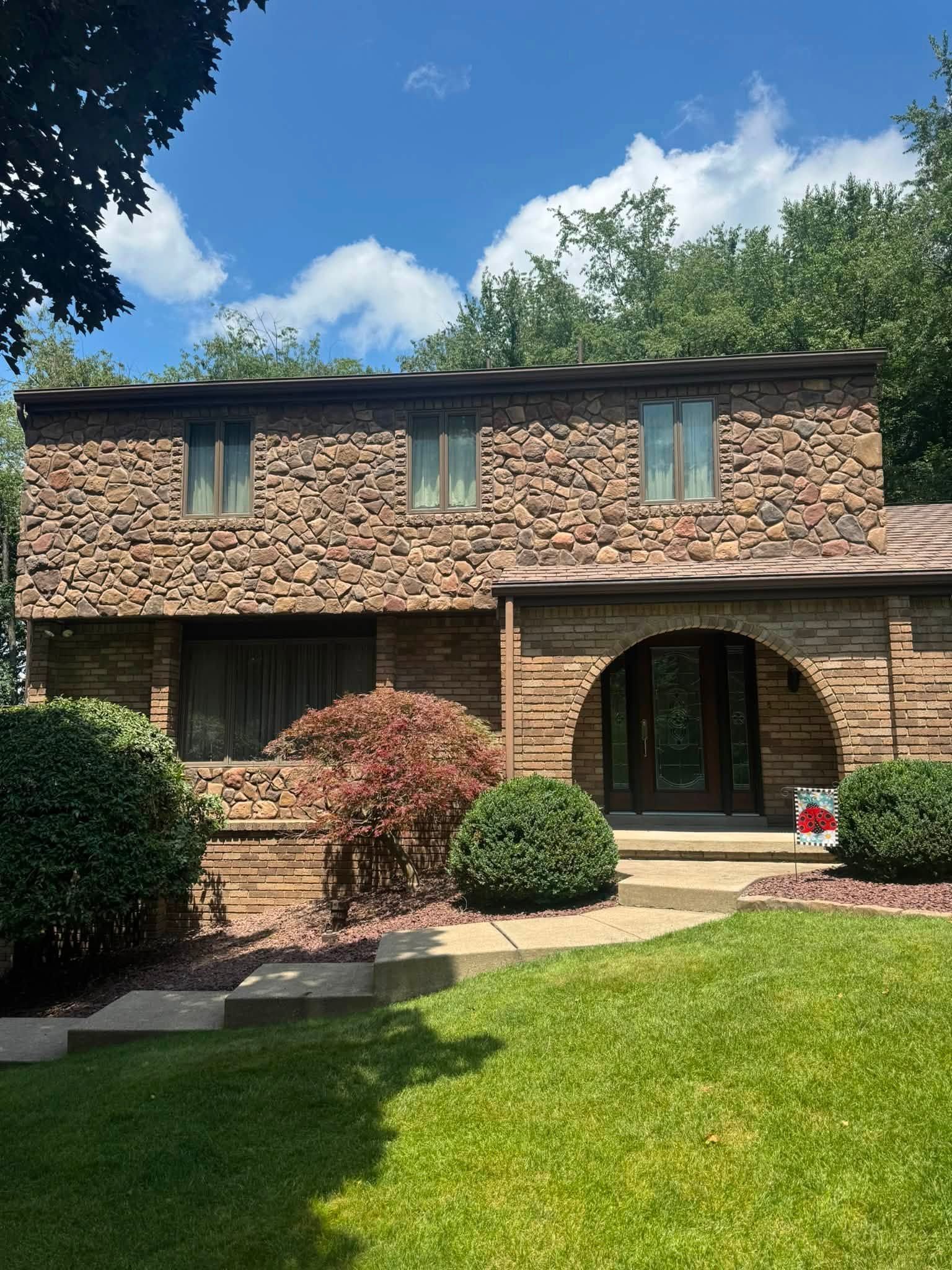Two-story brick house with arched front door, green lawn, and blue sky with clouds