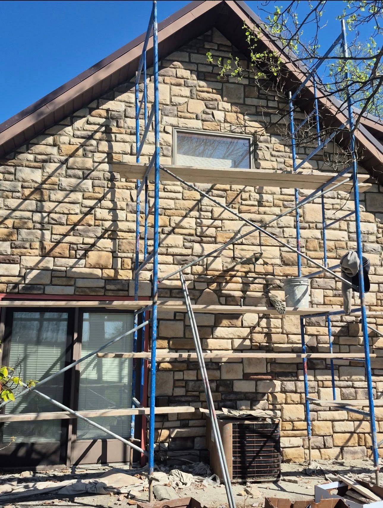 Stone house facade with scaffolding during exterior renovation under a clear blue sky