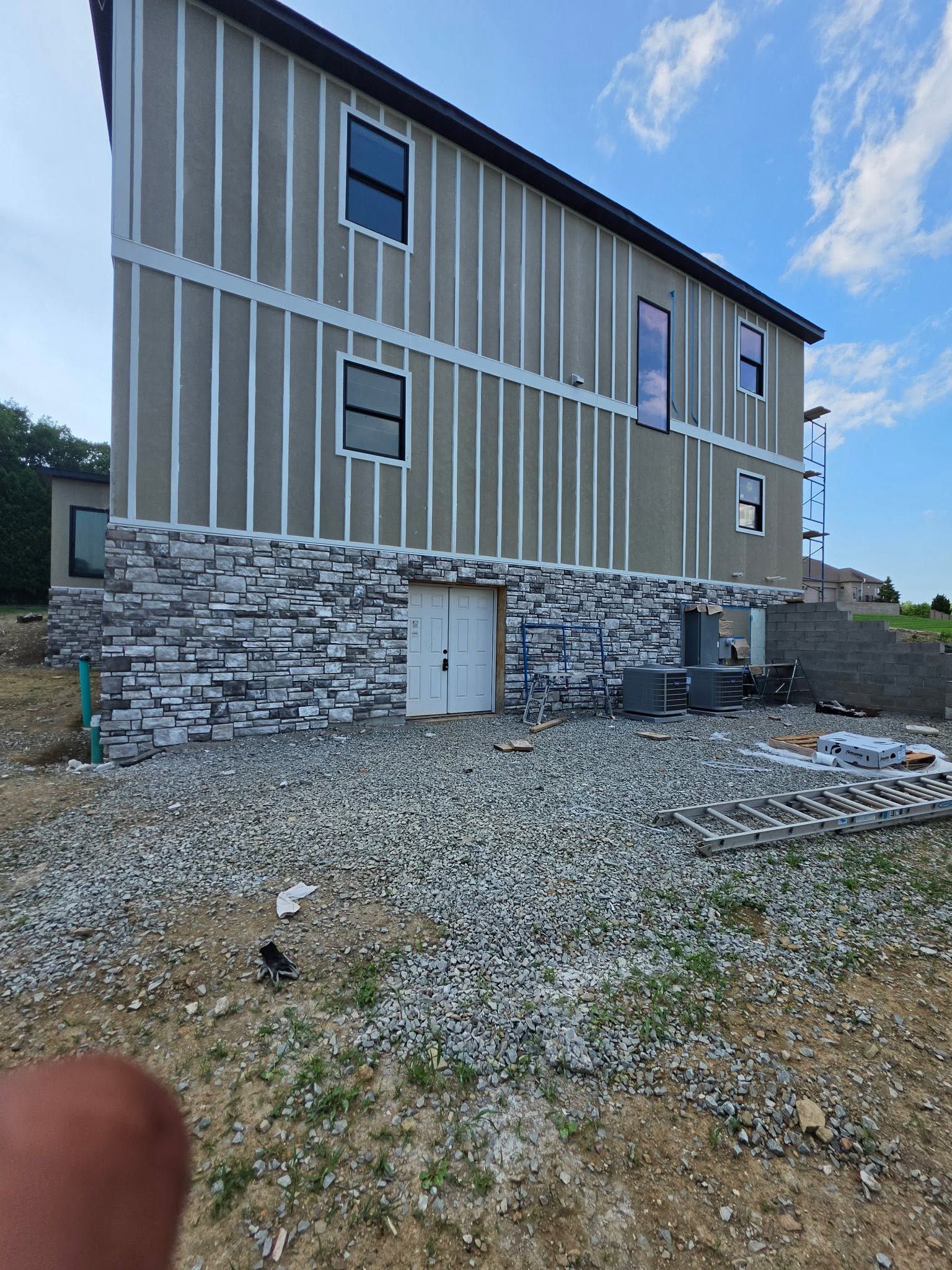 Two-story house with vertical siding and stone lower facade on a gravel lot, viewed from below