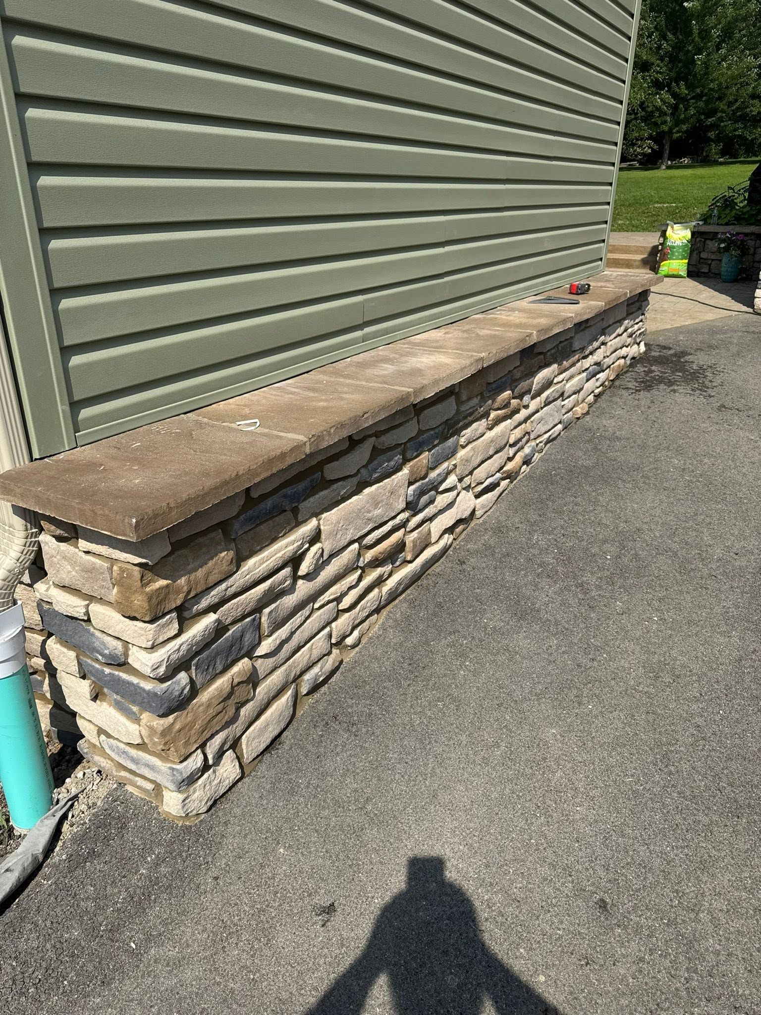 Stone bench along a green house wall beside a driveway in bright sunlight