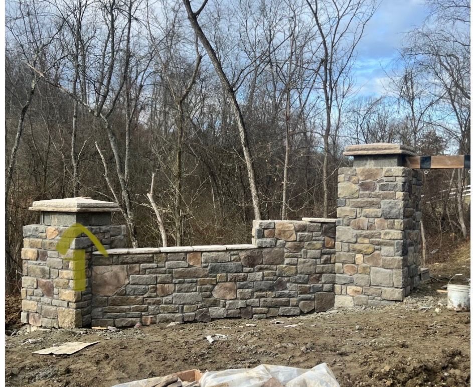 Stone fence and pillars under construction beside a wooded area in winter