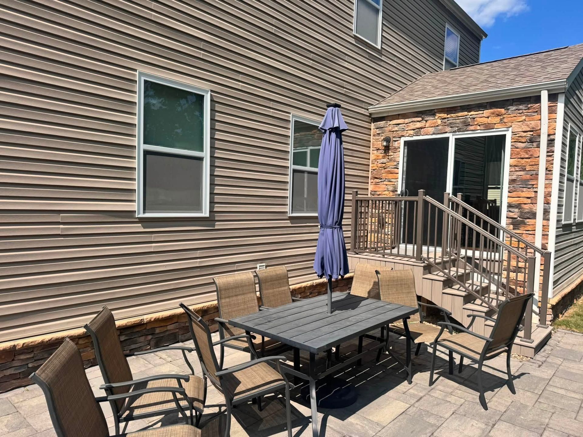 Backyard patio with outdoor dining table, chairs, closed umbrella, and sliding glass doors beside a house