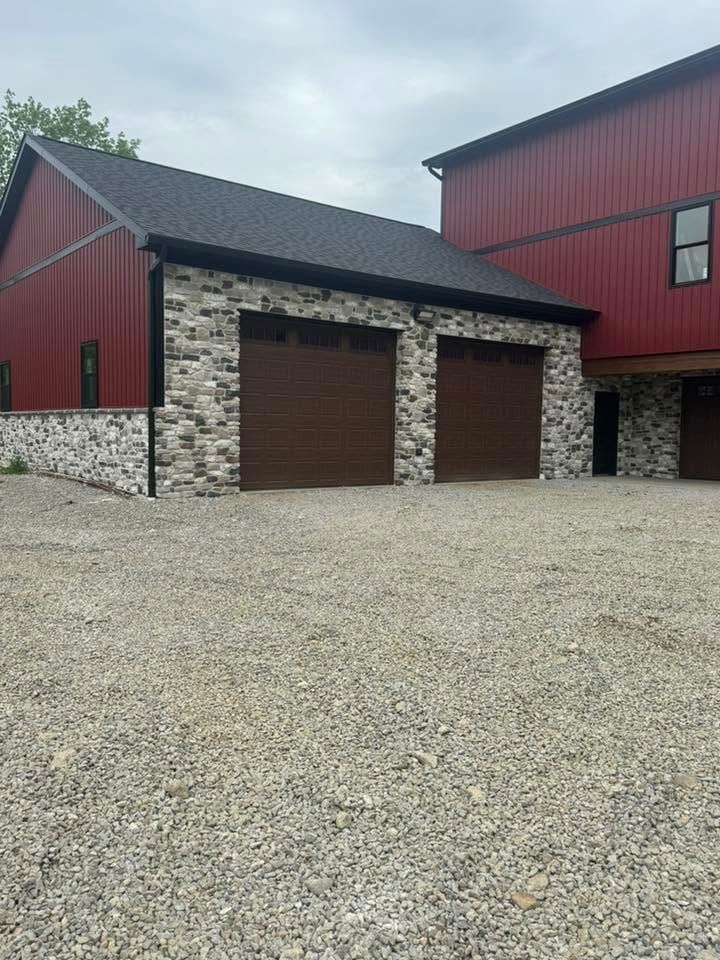 Red barn-style building with stone garage bays and gravel driveway under a cloudy sky