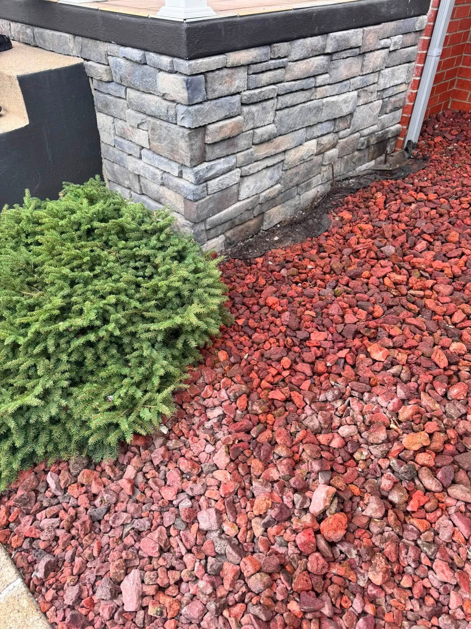 Landscaped corner with gray stone wall, green shrub, and red mulch ground cover.
