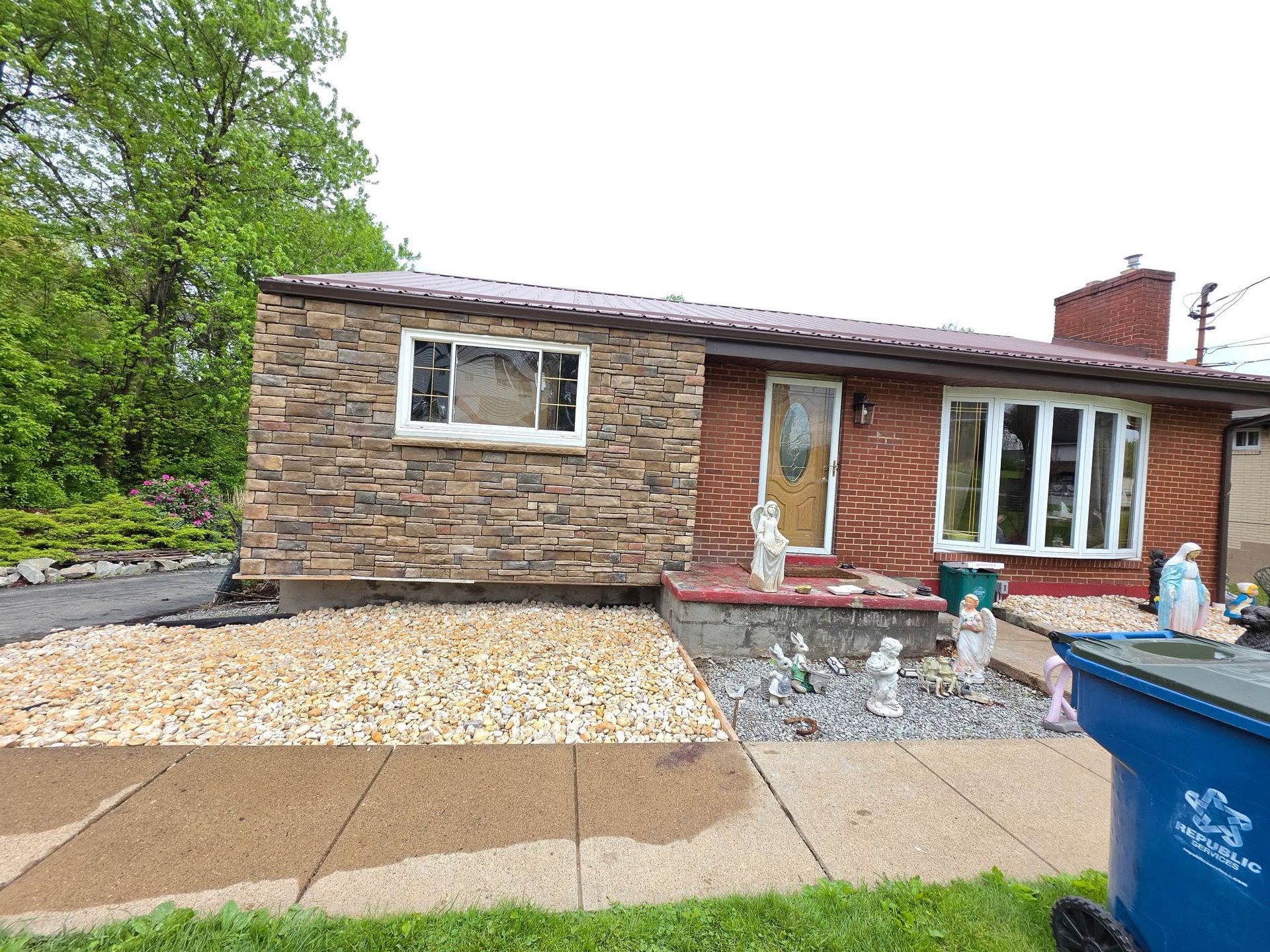 Single-story brick house with white-trimmed windows, front sidewalk, and gravel yard