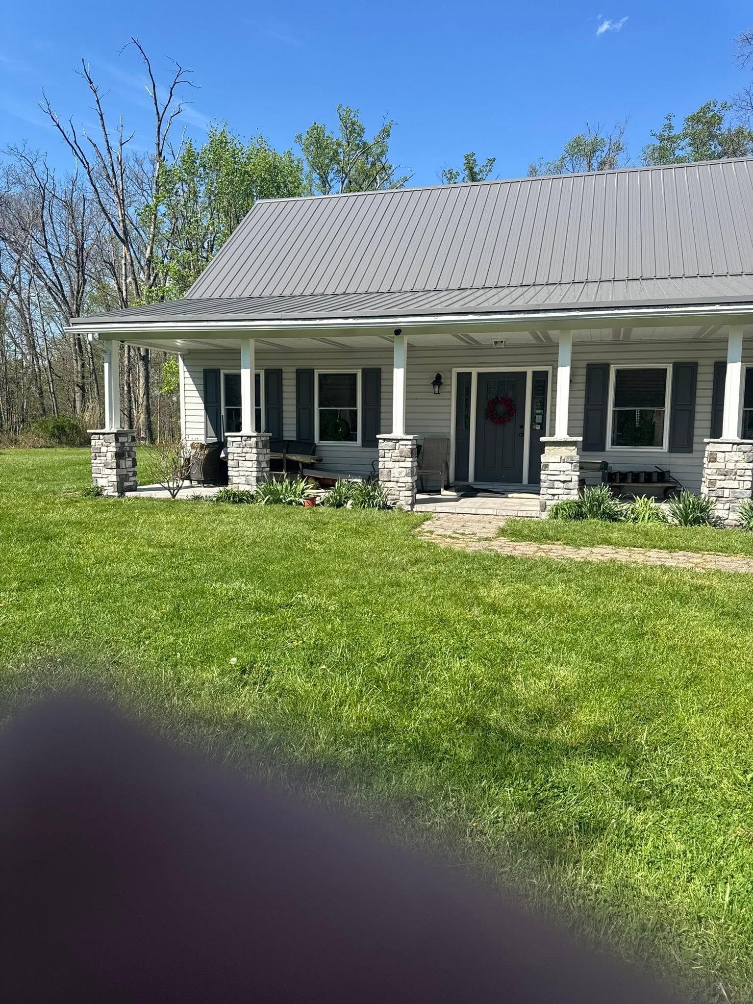 Single-story house with a gray roof, white porch columns, and a green lawn under a clear blue sky
