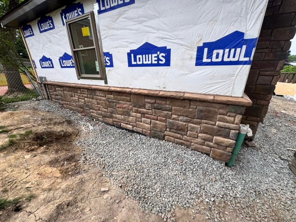 House exterior under construction with Lowe’s wrap, stone veneer, gravel, and a window frame