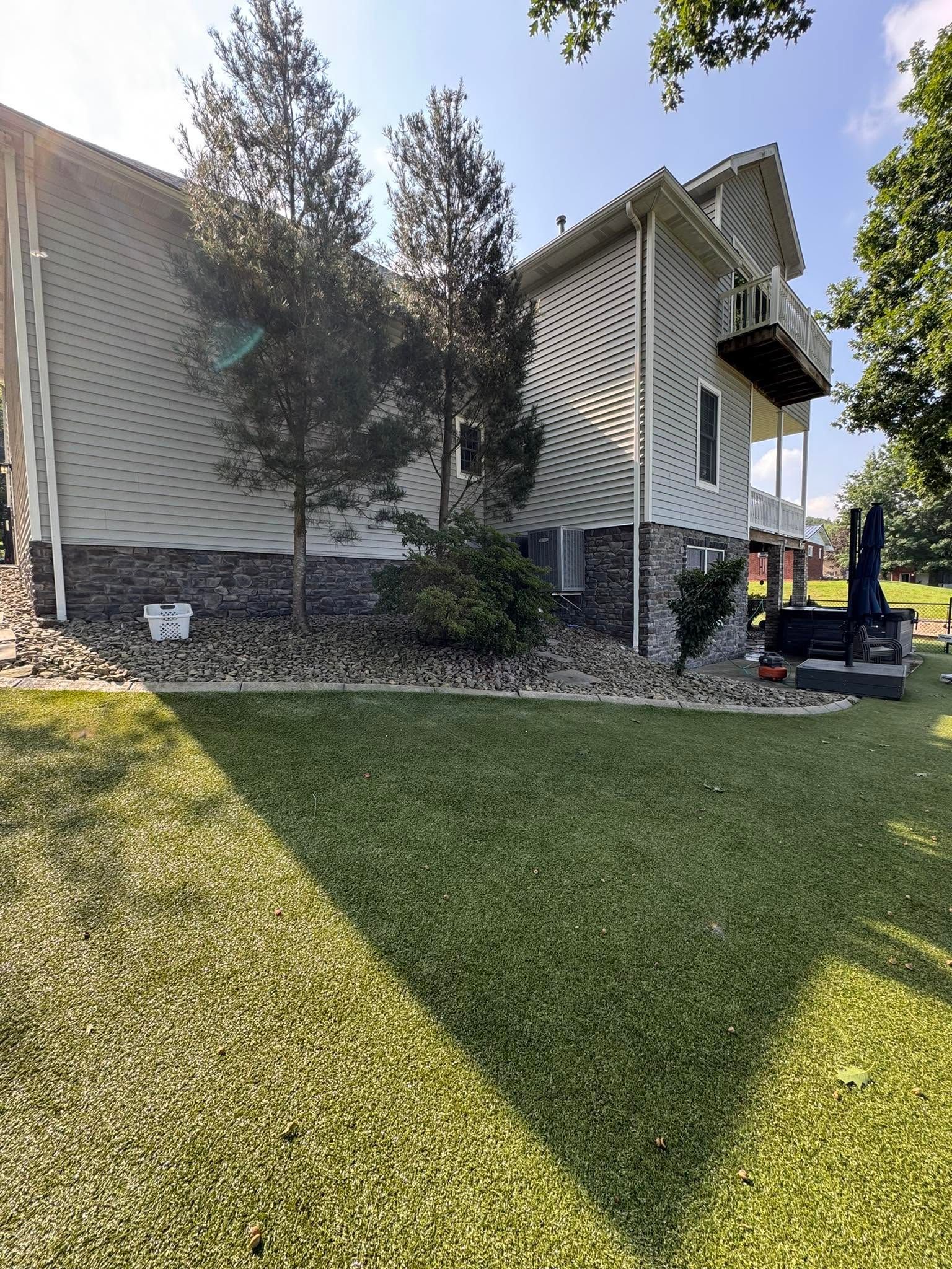 Residential building with beige siding, trees, and a manicured lawn in sunlight